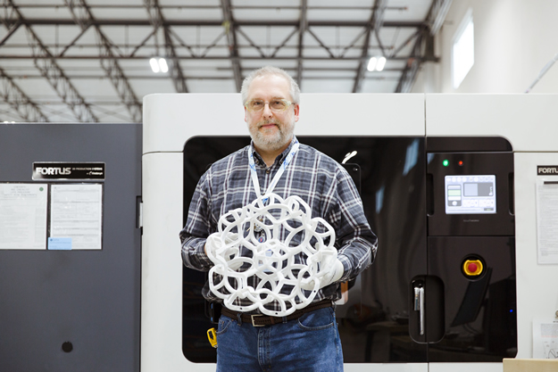 Rowley is holding the finished product in front of a polymer 3D printer. Image credit: GE Reports/Chris New